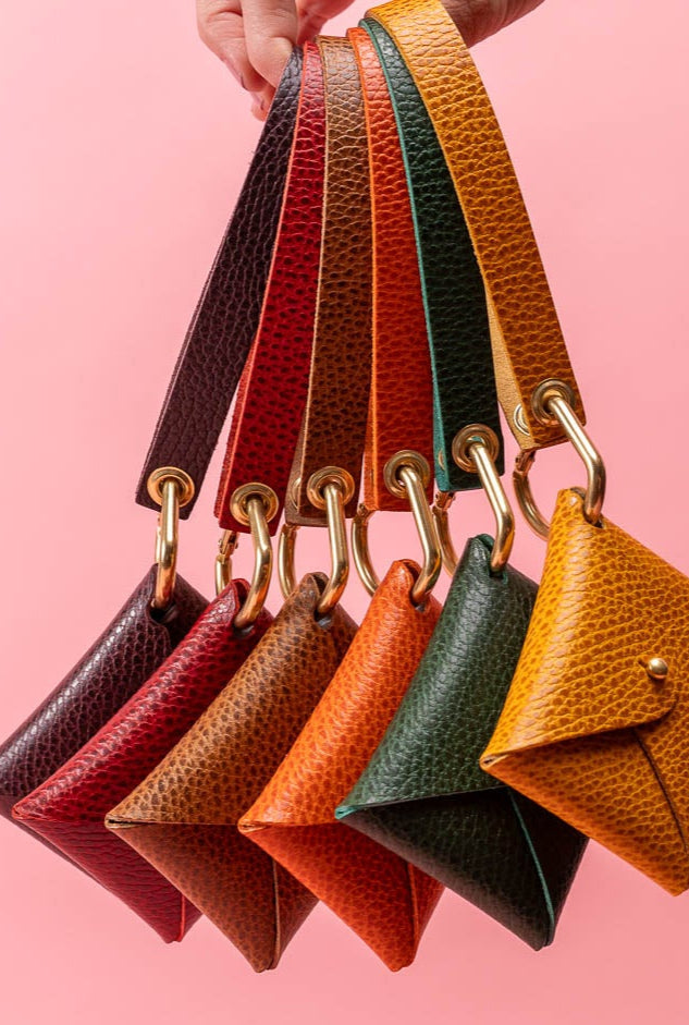 Set of colorful leather keychains held against a pink background