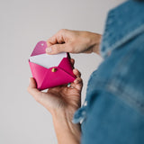 Person holding a pink wallet with a white interior against a neutral background